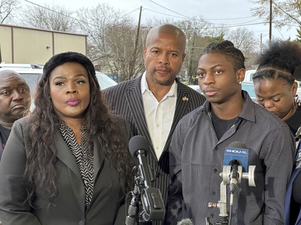 Daryl George, Jr., 18, along with his attorney, Ali Booker, left, and Texas state Rep. Ron Reynolds, center, talk to reporters Wednesday, Jan. 24, 2024, before a court hearing in Anawak, Texas on whether his school district in the Houston can continue to punish him for refusing to change his hairstyle.  A judge on Wednesday ordered a trial next month to determine whether George can continue to be penalized by his district for refusing to change his hairstyle, which he and his family say is protected by a new state law.  (AP Photo/Juan A. Lozano)