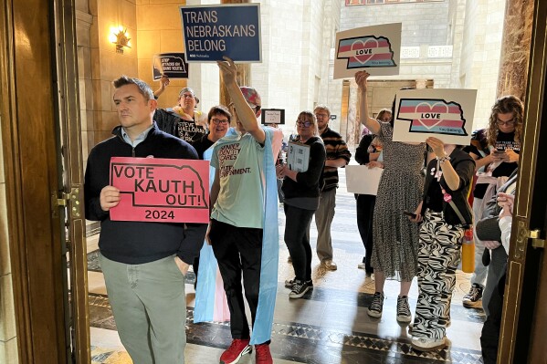 FILE - Protesters hold signs outside the doors of the legislative chamber in the Nebraska Capitol in response to a bill that would have restricted students to bathrooms, locker rooms and sports teams that correspond with the gender they were assigned at birth, April 5, 2024, in Lincoln, Neb. In a lawsuit filed Monday, April 29, four Republican state attorneys general are challenging a federal regulation that seeks to protect the rights of transgender students in the nation's schools by banning blanket policies that bar transgender students from school bathrooms aligning with their gender, among other provisions. (AP Photo/Margery Beck, File)