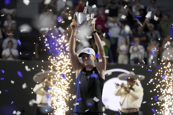FILE - Poland's Iga Swiatek holds her trophy after her victory over Jessica Pegula, of the United States, in the women's singles final of the WTA Finals tennis championships, in Cancun, Mexico, Monday, Nov. 6, 2023. Swiatek’s second consecutive season-ending No. 1 ranking helped her collect a second consecutive WTA Player of the Year award on Monday, Dec. 11, 2023, making her the first woman since Serena Williams to claim that honor twice in a row. (AP Photo/Fernando Llano, File)