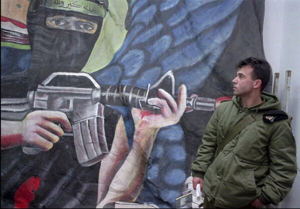 FILE - An Israeli soldier stands next to a Hamas propaganda poster seized during recent raids, at an Israeli army base in Hebron, March 7, 1996. (AP Photo/ Jacqueline Arzt, File)