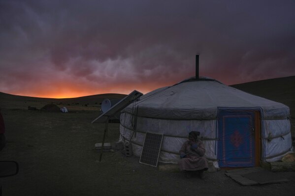 An assistant herder for Lkhaebum smokes a cigarette sitting outside a ger after a sudden dust storm at dusk in the Munkh-Khaan region of the Sukhbaatar district, in southeast Mongolia, Saturday, May 13, 2023. Weather extremes are a part of life in Mongolia, and managing them is increasingly difficult as the environment changes. (AP Photo/Manish Swarup)