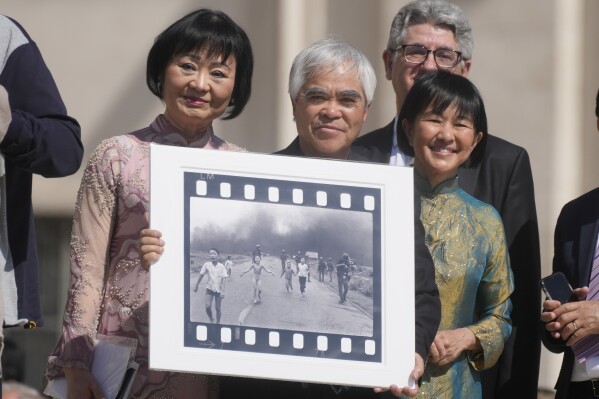 Pulitzer Prize-winning photographer Nick Ut, center, flanked by Kim Phuc, left, holds the" Napalm Girl", his Pulitzer Prize winning photo as they wait to meet with Pope Francis during the weekly general audience in St. Peter's Square at The Vatican, May 11, 2022. (AP Photo/Gregorio Borgia, file)