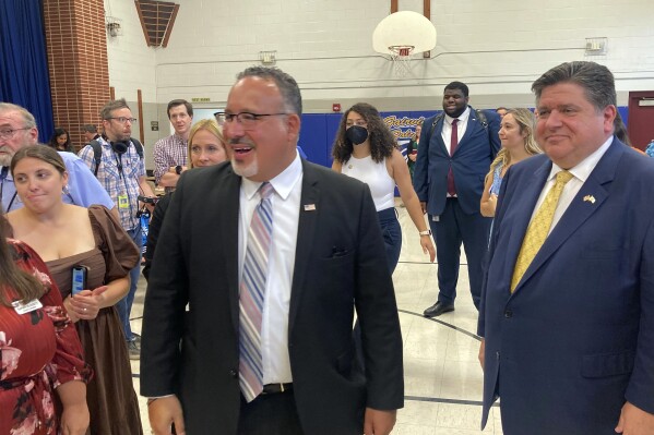 U.S. Education Secretary Miguel Cardona, left, and Illinois Gov. J.B. Pritzker, right, visit Fairview Elementary School in Springfield, Ill., on Wednesday, Sept. 6, 2023, interacting with students in the district's after-school program. Cardona is on a five-state Midwestern bus tour to tout the Biden administration's "Raise the Bar: Lead the World" education agenda. (AP Photo/John O'Connor)