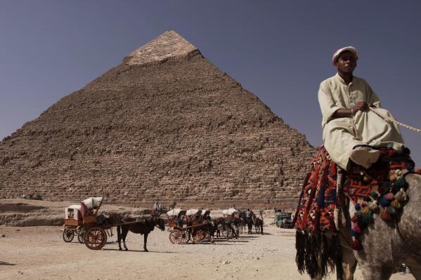 FILE - An Egyptian camel owner waits for customers to take a ride, in front of the Khafre pyramid, near Cairo, Egypt, Oct. 11, 2012.  An Egyptian court on Thursday, April 21, 2022, sentenced a former member of parliament and four others to ten years in prison and 17 others to five years in prison. for smuggling antiquities out of the country. Egypt has drastically stepped up efforts in recent years to stop the trafficking of its antiquities, which flourished in the turmoil following a 2011 uprising that toppled longtime autocratic leader Hosni Mubarak. (AP Photo/Nariman El-Mofty, File)
