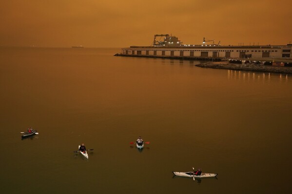 FILE - People in kayaks paddle in McCovey Cove outside Oracle Park in San Francisco during a baseball game between the San Francisco Giants and the Seattle Mariners on Sept. 9, 2020. As Earth's climate continues to change from heat-trapping gases spewed into the air, ever fewer people are out of reach from the billowing and deadly fingers of wildfire smoke, scientists say. (AP Photo/Tony Avelar, File)