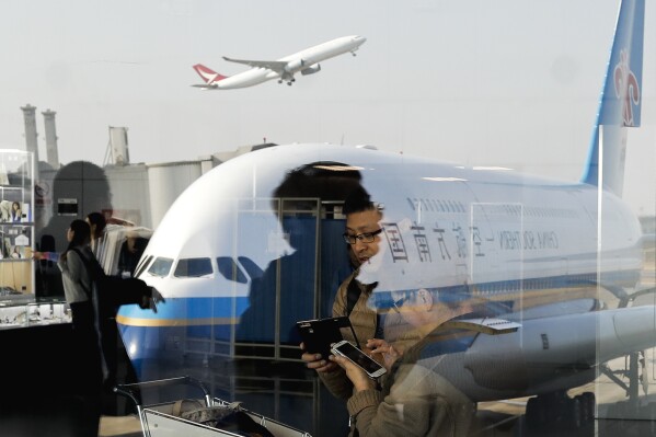 FILE - Passengers walk past a couple browsing their smartphones near a China Southern Airlines, parked on the tarmac at the Beijing Capital International Airport Saturday, Nov. 19, 2016. China’s Commerce Ministry said Thursday, May 30, 2024, it will restrict exports of aviation and aerospace-related equipment and technology beginning July 1, 2024.(AP Photo/Andy Wong, File)