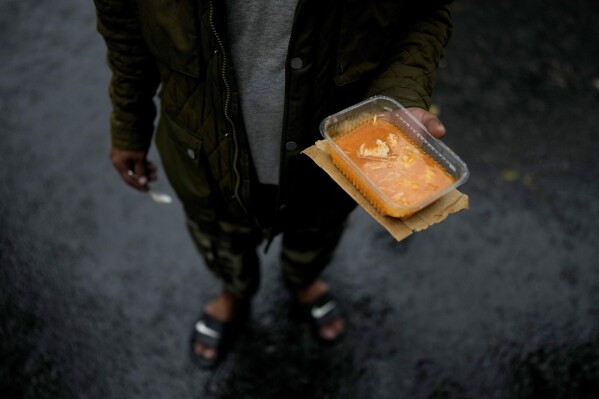 A resident holds a container of chicken stew that he received from the Excluded Workers Movement soup kitchen, in Buenos Aires, Argentina, March 13, 2024. Organizers said the kitchen is open three days a week and serves about 4,000 people a day, but because of the increasing number of people coming for meals, they often don't have enough to go around. (AP Photo/Natacha Pisarenko)