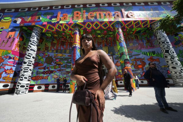 Brazilian artist Manauara Clandestina poses in front of the main entrance of the main pavilion at the 60th Biennale of Arts exhibition in Venice, Italy, Tuesday, April 16, 2024. The Venice Biennale contemporary art exhibition opens Saturday for its six-month run through Nov. 26. (AP Photo/Luca Bruno)