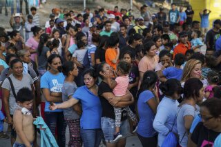 FILE - In this Aug. 30, 2019, file photo, migrants, many of whom were returned to Mexico under the Trump administration's "Remain in Mexico" policy, wait in line to get a meal in an encampment near the Gateway International Bridge in Matamoros, Mexio. The Biden administration on Friday, Feb. 12, 2021, announced plans for tens of thousands of asylum-seekers waiting in Mexico for their next immigration court hearings to be released in the United States while their cases proceed. (AP Photo/Veronica G. Cardenas, File)