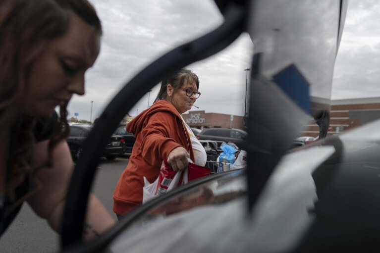 Jesse Johnson, left, of the Family Resource Center helps her client Jodi Ferdinandsen load groceries into the trunk at Walmart in Findlay, Ohio, Thursday, Oct. 12, 2023, before driving her home. (AP Photo/Carolyn Kaster)