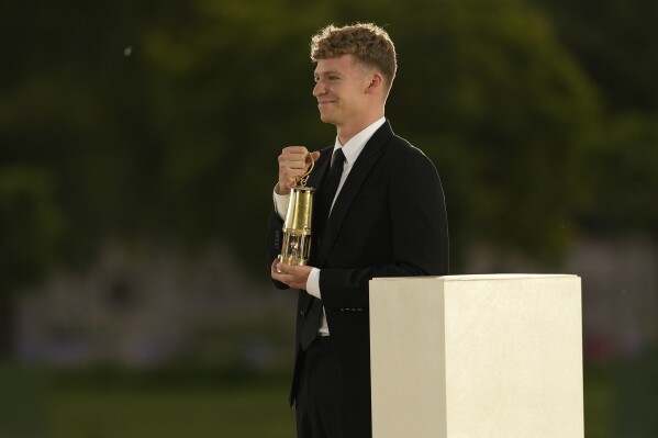 French swimmer Leon Marchand carries a lantern containing the Olympic flame in the Tuileries garden on the final day of the 2024 Summer Olympics ahead of the closing ceremony, Sunday, Aug. 11, 2024, in Paris, France. (AP Photo/Vadim Ghirda)