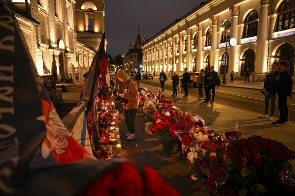 FILE - A young woman lights a candle as others stand at an informal street memorial near the Kremlin, in the background, in Moscow, Russia, on Tuesday, Aug. 29, 2023, for members of the Wagner Group of mercenaries who were killed in the crash of a private jet. Wagner chief Yevgeny Prigozhin and his top lieutenants were among the 10 people killed in the crash northwest of Moscow. (AP Photo/Alexander Zemlianichenko, File)