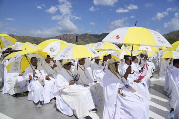 Faithful and priests use umbrellas with the colors of the Vatican flag to shield themselves from the sun as they wait for a mass presided over by Pope Francis to start in Tasitolu, some 8 kilometers west of Dili, East Timor, Tuesday, Sept. 10, 2024. Pope Francis presides over a mass in a seaside park on the same field where St. John Paul II celebrated a historic liturgy during East Timor's fight for independence from Indonesian rule. (AP Photo/Gregorio Borgia)