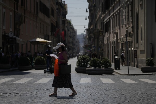 FILE - A woman waves her fan as she walks in downtown Rome, Aug. 22, 2023. UN weather agency says Earth sweltered through the hottest summer ever as record heat in August capped a brutal, deadly three months in northern hemisphere. (AP Photo/Gregorio Borgia, File)