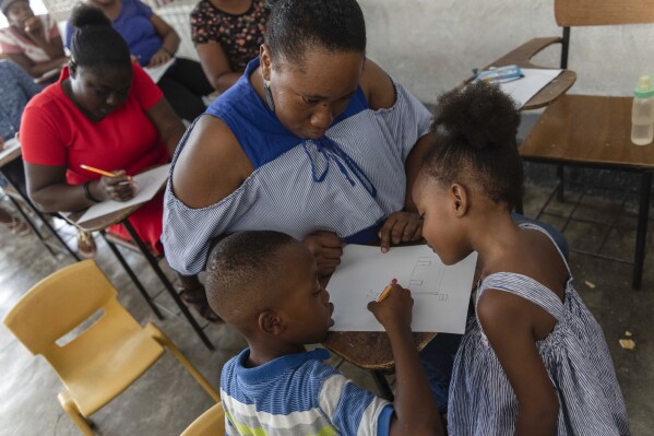 Guirlaine Reveil watches her son Jadlenzky Louis write about a drawing she made during a class for adults to teach parents how to help their children overcome trauma and fear amid violence, in Port-au-Prince, Haiti, Sunday, May 5, 2024. At right is her daughter Nhora Lynn Fedorat Louis. As young Haitians are increasingly exposed to violence, the country is undergoing a wider push to dispel a long-standing taboo on seeking therapy and talking about mental health. (AP Photo/Ramon Espinosa)