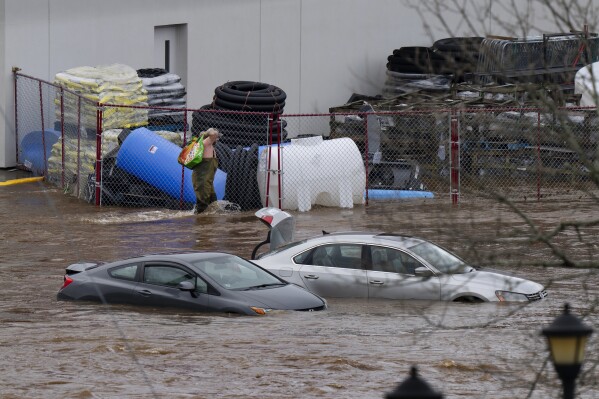 A man wearing chest waders walks past cars abandoned in floodwaters in a mall parking lot following a major rain event in Halifax, Nova Scotia, Canada, on Saturday, July 22, 2023. (Darren Calabrese/The Canadian Press via AP)