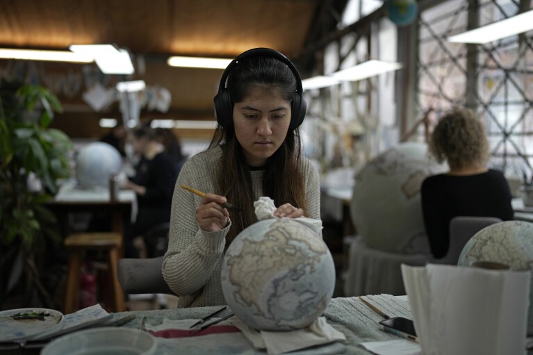 An artist paints a globe at a studio in London, Tuesday, Feb. 27, 2024. Globes in the age of Google Earth capture the imagination and serve as snapshots of how the owners see the world and their place in it. Peter Bellerby made his first globe for his father, after he could not find one accurate or attractive enough. In 2008, he founded Bellerby & Co. Globemakers in London. His team of dozens of artists and cartographers has made thousands of bespoke globes up to 50 inches in diameter. The most ornate can cost six figures. (AP Photo/Kin Cheung)