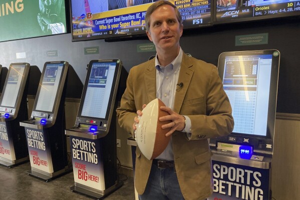 FILE - Kentucky Gov. Andy Beshear stands in front of sports betting kiosks at Churchill Downs, Sept. 7, 2023, in Louisville, Ky. Sports betting in Kentucky is off to a strong start right out of the gate, attracting more than $4.5 million in wagering since launching two weeks ago, Beshear said Thursday, Sept. 21. (AP Photo/Bruce Schreiner, File)