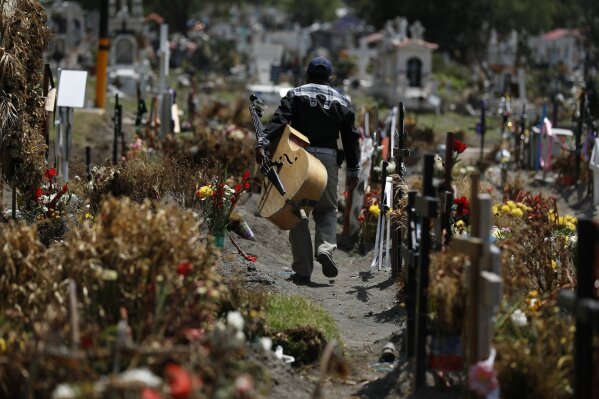 A musician walks between graves of people deceased in the last two months, in a section of the Municipal Cemetery of Valle de Chalco opened to accommodate the surge in deaths amid the ongoing coronavirus pandemic, on the outskirts of Mexico City, Thursday, July 2, 2020. (AP Photo/Rebecca Blackwell)