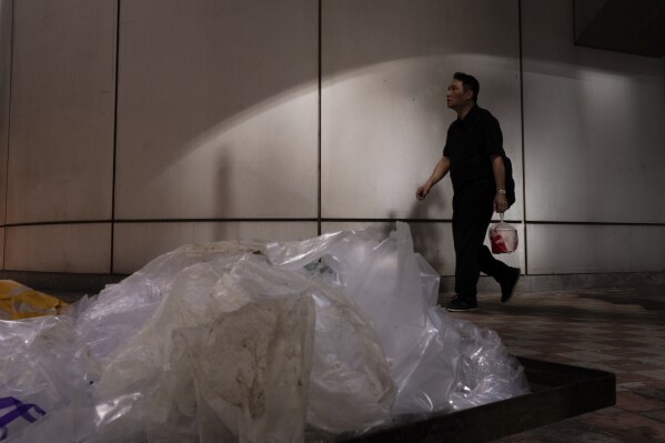 A pedestrian carrying takeaway food plastic bag walks past plastic waste in Hong Kong, Thursday, Feb. 21, 2024. Hong Kong has long been a major producer and consumer of great food, and a great amount of plastic and Styrofoam to go with it. That’s going to change as new legislation aiming to stop the sale and distribution of Styrofoam products and single-use plastic cutlery went into effect on Monday, April 22, 2024.(AP Photo/Louise Delmotte)