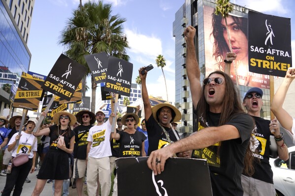 File - SAG-AFTRA member John Schmitt, second from right, and others carry signs on the picket line outside Netflix on Wednesday, Sept. 27, 2023, in Los Angeles. Saturday marks the 100th day that film and TV performers from the Screen Actors Guild-American Federation of Television and Radio Artists have been on strike, seeking changes to compensation and protections from use of artificial intelligence in their craft. (AP Photo/Chris Pizzello, File)