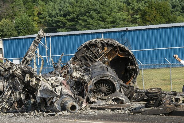 FILE - In this Aug. 16, 2019, file photo, a member of the National Transportation Safety Board looks at the wreckage of a plane that Dale Earnhardt Jr., his wife and daughter and two pilots and a dog were on when it crash landed at the Elizabethton Municipal Airport in Elizabethton, Tenn. Earnhardt Jr. and a pilot struggled to open a crashed airplane's rear exit door as the aircraft began to burn and fill with smoke before the race car driver and his family managed to escape from the main door, according to new details about the 2019 accident released by the National Transportation and Safety Board.(David Crigger/Bristol Herald Courier via AP, File)