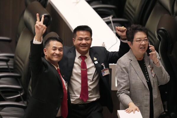 Leader of Pheu Thai party Chonlanan Srikaew, left, and his party lawmakers make victory signs at Parliament in Bangkok, Thailand, Tuesday, Aug. 22, 2023, after securing enough votes in parliament for their nominee Srettha Thavisin to become Thailand's 30th prime minister. (AP Photo/Sakchai Lalit)