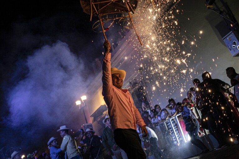 People parade with fireworks during the Guelaguetza festival in Oaxaca, Mexico, late Saturday, July 15, 2023. During the government-sponsored event, 16 Indigenous ethnic groups and the Afro-Mexican community promote their traditions through public dances, parades and craft sales. (AP Photo/Maria Alferez)