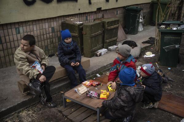 Children sit around a small table with snacks they received in a free food delivery in Bucha, on the outskirts of Kyiv, Ukraine, Friday, April 8, 2022. The graffiti written by the neighbors on the wall in background reads "Children", to inform Russian military that many children live in the building. (AP Photo/Rodrigo Abd)