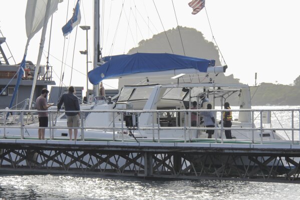 Relatives stand nearby as investigators from Grenada and St. Vincent and the Grenadines stand aboard the yacht 