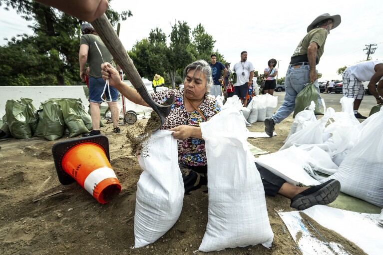 Sentada en el suelo, Norma Panilla empaqueta meticulosamente sacos de arena en Wildwood Park en San Bernardino, California, el sábado 19 de agosto de 2023, mientras se prepara para proteger su hogar de posibles inundaciones que se esperan con la inminente llegada del huracán Hilary.  (Watchara Phomicinda/The Orange County Register vía AP)