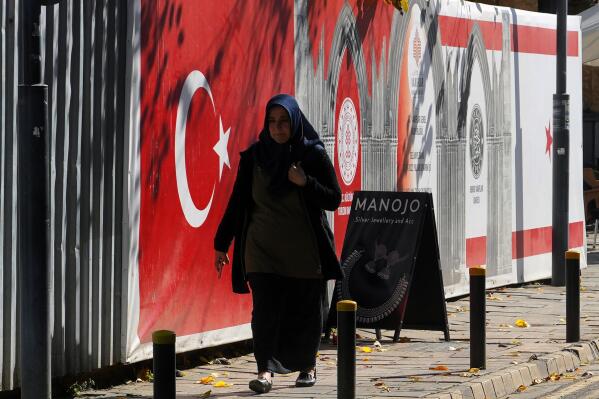 A woman wearing her headscarf walks by a Turkish flag on a print board, in a street in the old city of the Turkish occupied part of the divided capital Nicosia, Cyprus, Wednesday, Jan. 18, 2023. A Muslim religious leader's exhortation to women that they're duty bound to accept their husband's "invitation to bed" to procreate has sparked outrage among many Turkish Cypriots who saw the remarks as a further encroachment of Turkish-imported fundamentalist Islam on their secular community. (AP Photo/Petros Karadjias)