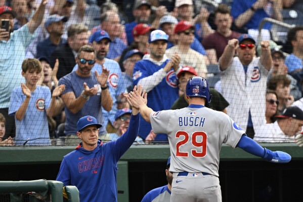 Chicago Cubs manager Craig Counsell, left, greets Michael Busch (29) after he scored a run on a sacrifice fly hit by Dansby Swanson against Washington Nationals pitcher Trevor Williams during the second inning of a baseball game in Washington, Tuesday, June 3, 2025. (AP Photo/Terrance Williams)