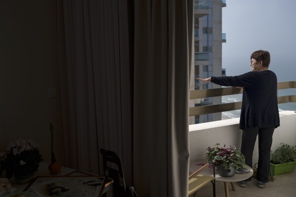 Tami Halevi, 86, stands on the balcony of the apartment in an assisted living facility in Bat Yam, Israel, Friday, Feb. 9, 2024, where she is staying after leaving her house in Kibbutz Nahal Oz. (AP Photo/Leo Correa)
