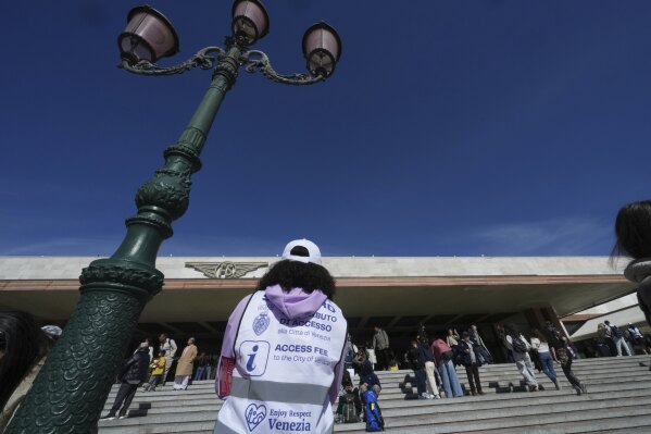 Stewards check tourists' QR codes outside the main train station in Venice, Italy, Friday, April 18, 2025, as the city for a second year is charging day-trippers an arrivals tax. (AP Photo/Antonio Calanni)