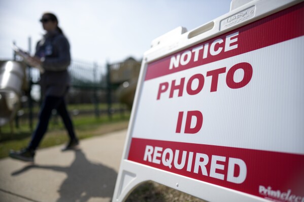 FILE - A Super Tuesday voter walks past a sign requiring a photo ID at a polling location, March 5, 2024, in Mount Holly, N.C. A federal lawsuit challenging North Carolina's photo voter identification law goes to trial Monday, May 6, with expected arguments focusing on whether the requirement unlawfully discriminates against Black and Hispanic citizens or serves legitimate state interests to boost public confidence in elections. (AP Photo/Chris Carlson, File)