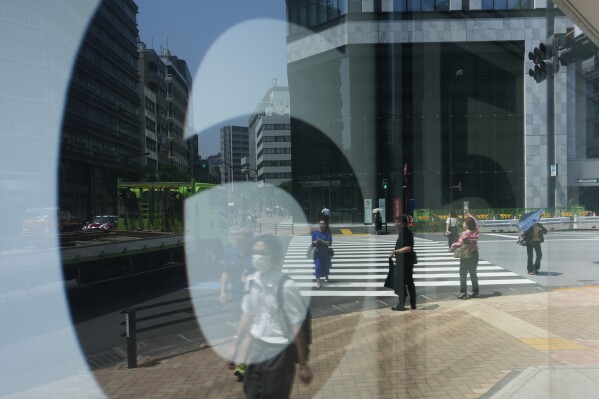 People walk across an intersection near monitors showing Japan's Nikkei 225 index at a securities firm in Tokyo, Thursday, July 27, 2023. Asian shares were mixed on Friday after the Bank of Japan adjusted its bond purchase policy but kept its negative benchmark interest rate unchanged. (AP Photo/Hiro Komae)