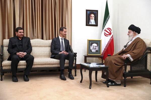 In this photo released by the official website of the office of the Iranian supreme leader, Supreme Leader Ayatollah Ali Khamenei, right, listens to Syrian President Bashar Assad, center, as Iranian acting President Mohammad Mokhber sits at left, in a meeting in Tehran, Iran, Thursday, May 30, 2024. Portraits of the late Iranian revolutionary founder Ayatollah Khomeini, top, and the late President Ebrahim Raisi are seen. (Office of the Iranian Supreme Leader via AP)