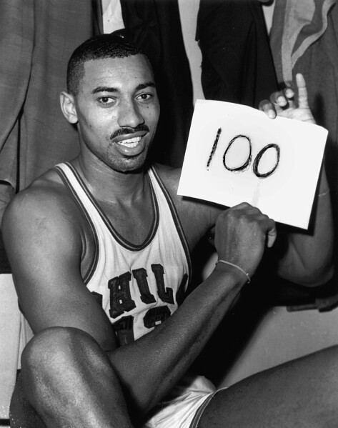 FILE - In this March 2, 1962 file photo, Wilt Chamberlain of the Philadelphia Warriors holds a sign reading "100" in the dressing room in Hershey, Pa., after he scored 100 points,  as the Warriors defeated the New York Knickerbockers 169-147. (AP Photo/Paul Vathis, File)