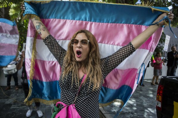 Lola Vazquez, who identifies as transgender, waves a transgender flag during a protest against a deal Guatemalan President Jimmy Morales' government signed with Washington that would force Salvadoran and Honduran migrants to request asylum in Guatemala instead of the United States, in Guatemala City, Wednesday, July 31, 2019. Critics of the deal point out that Guatemala has the same problems that are driving Hondurans and Salvadorans to flee their homes: violence, poverty, joblessness and a prolonged drought that has severely hurt farmers. (AP Photo/ Oliver de Ros)