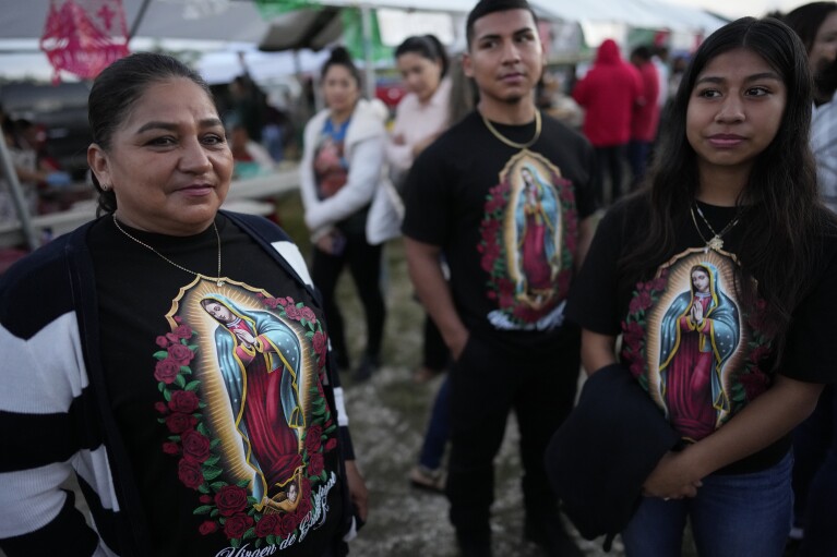 Members of a family wear matching shirts featuring images of the Virgin of Guadalupe, during a festival honoring one of several apparitions of the Virgin Mary witnessed by an indigenous Mexican man named Juan Diego in 1531, at St. Ann Mission in Naranja, Fla., before dawn on Sunday, Dec. 10, 2023. For this mission church where Miami's urban sprawl fades into farmland and the Everglades swampy wilderness, it's the most important event of the year, both culturally and to fundraise to continue to minister to the migrant farmworkers it was founded to serve in 1961. (AP Photo/Rebecca Blackwell)