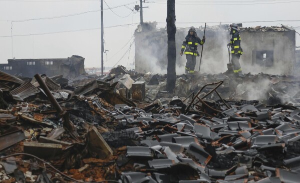 Firefighters look at the rubble and wreckage of a burned-out marketplace after a large fire caused by earthquakes in Wajima, Ishikawa prefecture, Japan Wednesday, Jan. 3, 2024. (Kyodo News via AP)