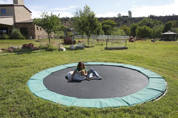 Suzy Elghanayan sits on a trampoline with Gretl, a pygmy goat, at the Selah Carefarm in Cornville, Ariz., Oct. 4, 2022. Her son, Luca, 20, died earlier in the year of a seizure. (AP Photo/Dario Lopez-Mills)