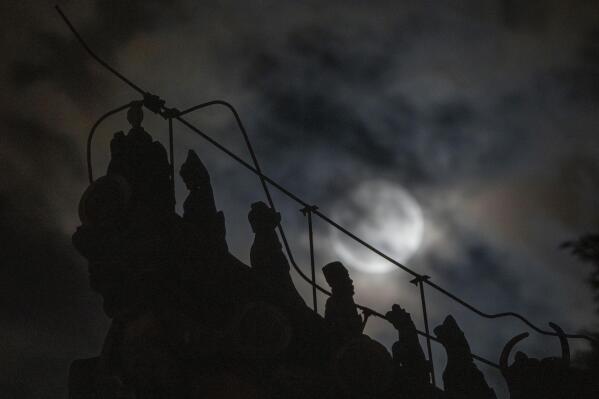 Roof decorations depicting mythical sacred beasts are silhouetted near a penumbral lunar eclipse partially blocked by clouds during the early hours of Saturday, May 6, 2023 in Beijing. (AP Photo/Ng Han Guan)