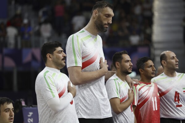 Irans's Morteza Mehrzadselakjani, fourth from right, stands with his teammates on the men's sitting volleyball team as the Iranian national anthem plays before their preliminary game against Brazil during the Paralympic Games in Paris, Sunday, Sept. 1, 2024. Iran won the game in straight sets. (AP Photo/Avni Trivedi)