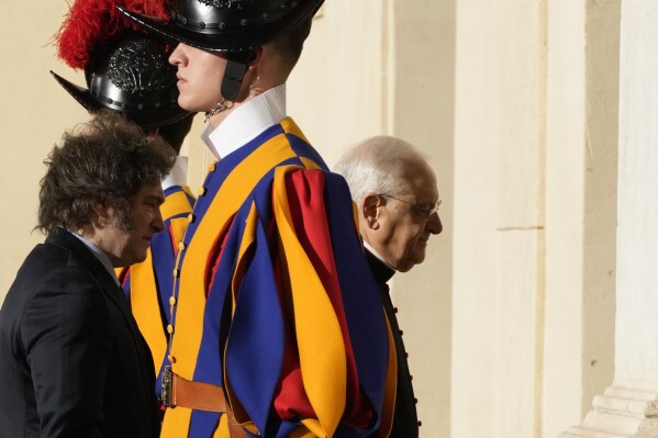 Argentine President Javier Milei, left, is preceded by the head of the Papal Household, Bishop Leonardo Sapienza, right, past two Pontifical Swiss Guards in the St. Damasus Courtyard at The Vatican as he arrives for a private audience with Pope Francis, Monday, Feb. 12, 2024. Milei, who will meet Italian President Sergio Mattarella and Italian Premier Giorgia Meloni later in the day, attended the canonization of the first Argentine female saint, María Antonia de Paz y Figueroa also known as "Mama Antula" in St. Peter's Basilica on Sunday. (AP Photo/Alessandra Tarantino)