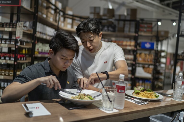 Darren Long, left, and Gerard Chia sample lab cultivated chicken from GOOD Meat during a tasting at Huber's Butchery in Singapore, Thursday, July 13, 2023. Singapore was the first nation to authorize the sale of meat cultured from cells in a bioreactor. A chef there offers a tasting menu every week. (AP Photo/David Goldman)