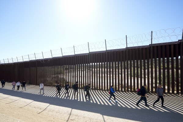FILE - A group of people, including many from China, walk along the wall after crossing the border with Mexico to seek asylum, Tuesday, Oct. 24, 2023, near Jacumba, Calif. As Congress returns this week, Senate Republicans have made it clear they won鈥檛 support additional war aid for Ukraine unless they can pair it with border security measures. (AP Photo/Gregory Bull, File)