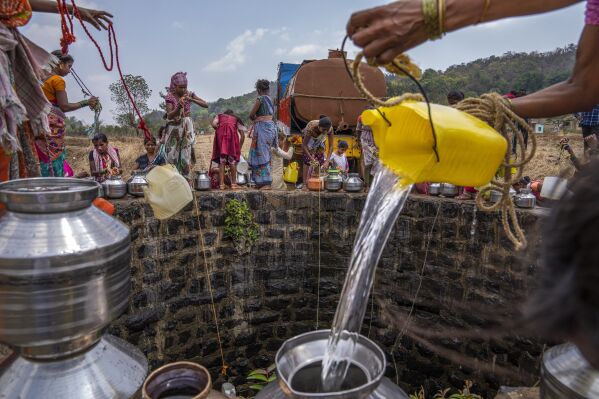 A villager pours water into a canister as others gather around a well to draw water in Telamwadi, northeast of Mumbai, India, Saturday, May 6, 2023. Tankers bring water from the Bhatsa River after it has been treated with chlorine. There have been protests in the region since so much of the river water is diverted to urban areas, including Mumbai. (AP Photo/Dar Yasin)