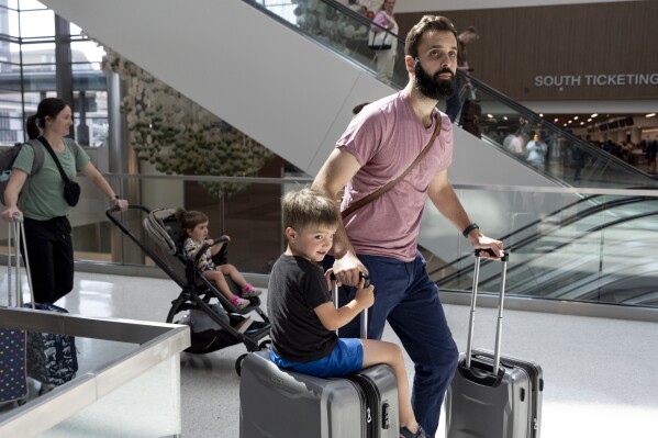 George Ridley (4 lata, po lewej) jedzie na walizce, gdy on i jego ojciec, Chris Ridley, przemierzają międzynarodowe lotnisko w Nashville, czwartek, 23 maja 2024 r., w Nashville w stanie Tennessee.  Oczekuje się, że rekordowa liczba Amerykanów będzie podróżować podczas weekendu z okazji Dnia Pamięci w 2024 r. (AP Photo/George Walker IV)